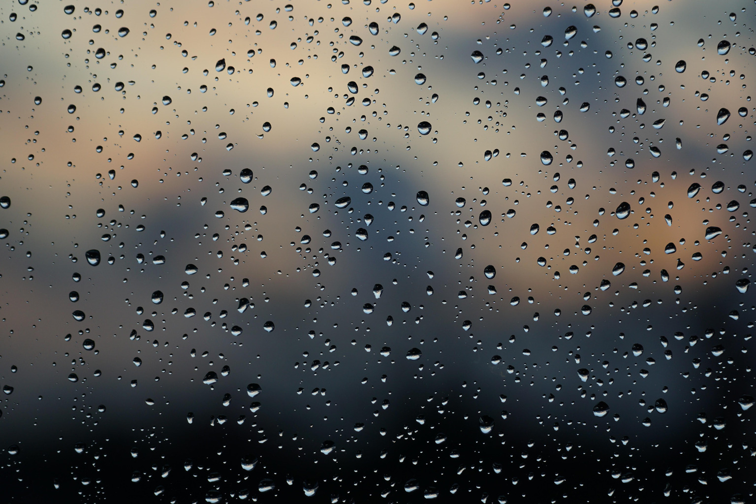 Raindrops on a window with a blurred outdoor view beyond the glass.